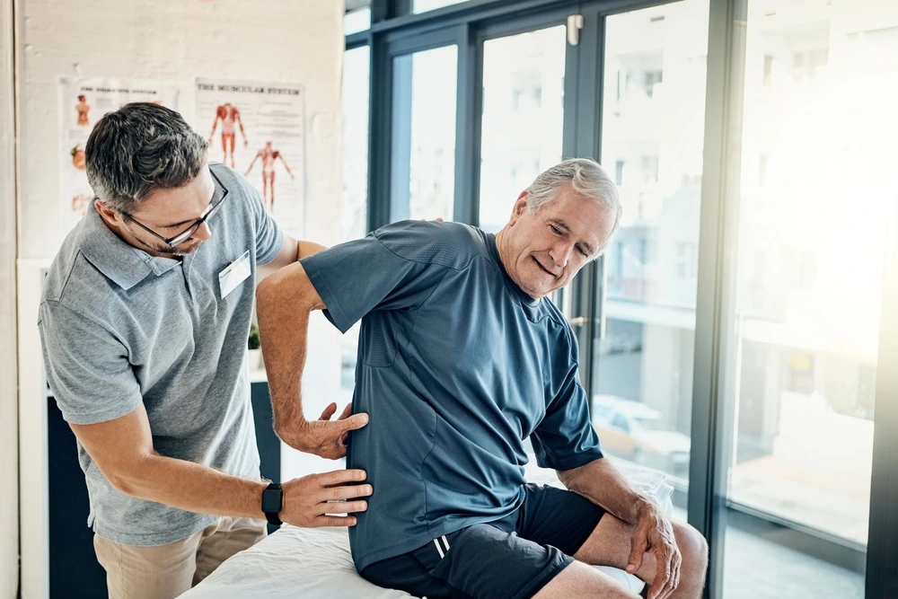 Older man receiving lower back pain treatment from chiropractor, showing benefits of massage therapy in Henderson and Las Vegas for auto accident injury and personal injury care